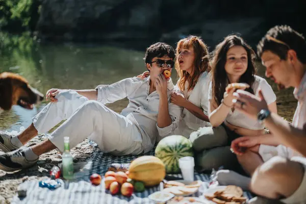 stock image A group of friends relaxes and shares a picnic by a lakeside, enjoying sunny weather, food, and companionship.