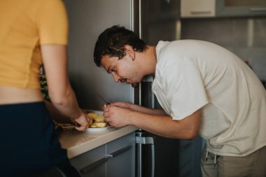 A young couple is preparing food in their modern kitchen. The man is focused on peeling apples while the woman assists, creating a cozy and collaborative atmosphere. clipart