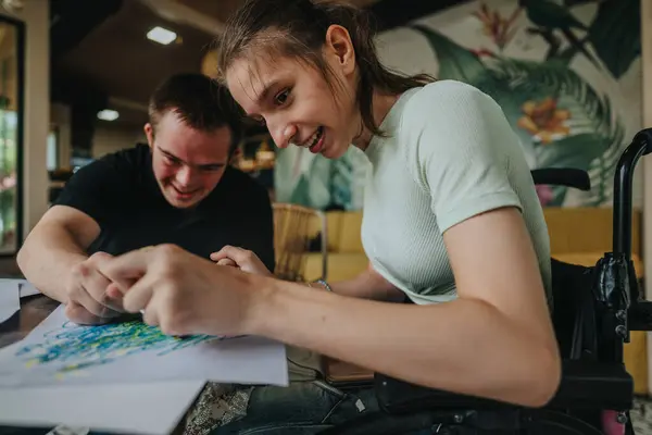 stock image A young man with Down syndrome and a girl in a wheelchair enjoy drawing and painting together, highlighting friendship and inclusion through art in a creative and supportive environment.