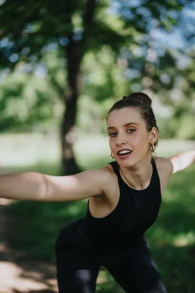 stock image Young woman in black workout attire performing modern dance in a lush green park, showcasing joy and freedom.