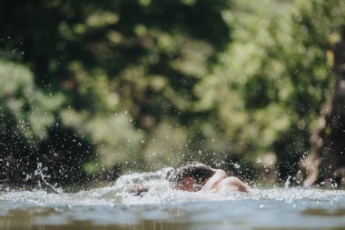 A person is swimming in a natural water body, creating splashes under the sunlight. The scene captures the essence of summer and outdoor adventure. clipart