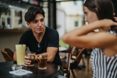 Two young adults share a candid conversation while enjoying refreshing drinks at a stylish cafe. The relaxed atmosphere promotes genuine connection and engagement. clipart