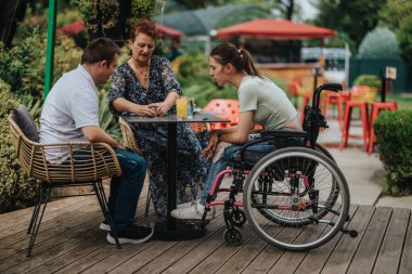 A boy with Down syndrome, a girl in a wheelchair, and an older woman enjoying a card game outdoors, bonding and having fun together. clipart