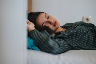 A young woman rests peacefully on a bed, wearing a striped pajama top. The serene setting conveys tranquility and relaxation, depicting a restful sleep in a calm environment. clipart