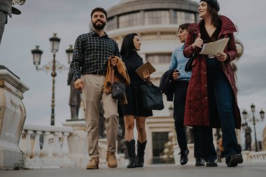 A diverse group of young professionals walks together in an urban area, showcasing confidence, teamwork, and a modern lifestyle against a backdrop of classic architecture. clipart