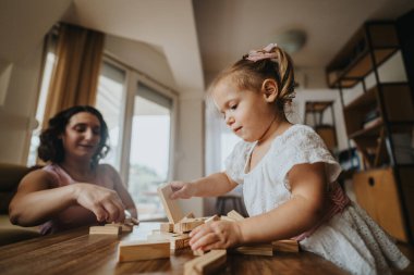 Mother and daughter playing with wooden blocks at a wooden table, showcasing a warm and educational family bonding moment in a cozy home. clipart