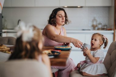 A mother is feeding her young daughters at a dining table in a cozy home kitchen, reflecting family bonding and nurturing. clipart