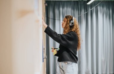 A dedicated student listens to music while writing on a board in a contemporary classroom, fostering creativity and focus. She exemplifies a blend of technology and traditional learning. clipart