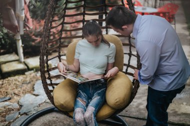 A boy with Down syndrome and a disabled girl share a moment reading together outdoors in a cozy garden chair. clipart