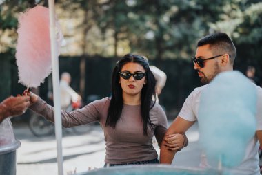 A young couple is seen enjoying cotton candy together at an outdoor summer festival. They are sharing a playful and lighthearted moment under the sunlight. clipart