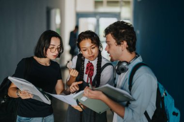 Three diverse students engage in an animated discussion, holding notebooks and textbooks, while standing in a busy school hallway. The scene captures academic collaboration and lively student clipart