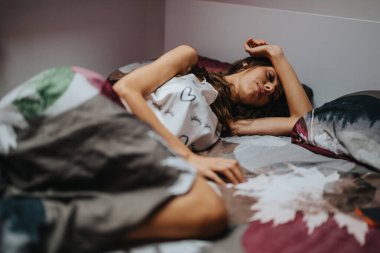 A woman wearing a patterned top lies comfortably in bed, surrounded by cozy sheets. She appears relaxed and peaceful, enjoying a moment of rest and tranquility in the bedroom. clipart