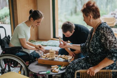 Heartwarming moment as a boy with Down syndrome, a girl in a wheelchair, and an elderly woman engage in a playful building blocks game, promoting inclusivity and inter generational bonding. clipart