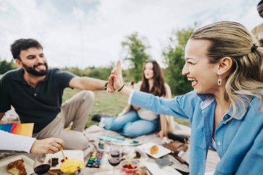 Group of friends having a joyful picnic in a park, sharing food and laughter. Two friends give each other a high five, capturing the essence of friendship and happiness. clipart