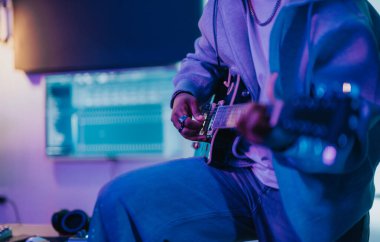 Musician skillfully plays an electric guitar in a vibrant, modern recording studio. The setup includes computer screens and headphones, creating an inspiring atmosphere for creative music production. clipart