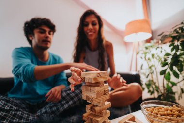 A young couple enjoys a fun and relaxed evening playing a wooden block stacking game together at home. The atmosphere is cozy and engaging, filled with laughter and excitement. clipart