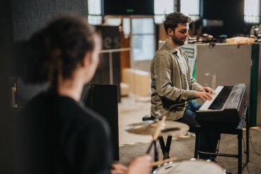 Two musicians practicing together, one playing the piano and another on the drums, preparing for a performance in a spacious and creative rehearsal environment. clipart