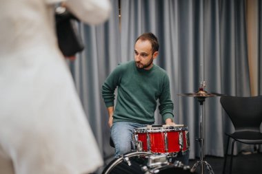 A drummer adjusts his red drum set while preparing for a music rehearsal session. clipart