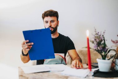 A focused college student studies at home, surrounded by books and notes. A red candle and potted plant add a cozy atmosphere to the workspace, fostering concentration and productivity. clipart