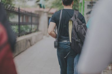 A man carrying a black backpack walks down a tree-lined city sidewalk. The image captures the urban environment and the casual activity of strolling in a public space. clipart