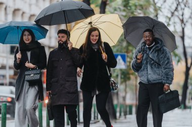 A cheerful group of individuals under umbrellas walking together through a city in the rain, enjoying their shared time outdoors, expressing camaraderie and resilience despite the weather. clipart