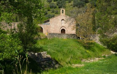 Assisi, Umbria bölgesi yakınlarındaki yeşil arazideki antik küçük kilise manzarası, İtalya