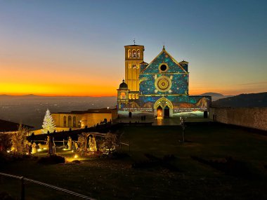 ASSISI, ITALY - 18 ARALIK 2023: Umbria bölgesinde romantik günbatımı ile Noel zamanı Assisi Aziz Francis Bazilikası manzarası