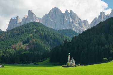 Santa Maddalena köyü Val Di Funes, İtalya 'da bulutlarla kaplı Geisler tepelerine karşı St. Johann Kilisesi' nin manzarası çok güzel.. 