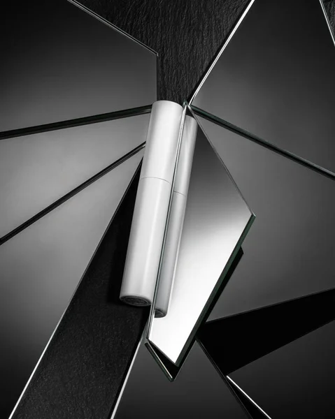 cosmetic mascara packaging on a background of mirrored feathering pieces on black textured stone