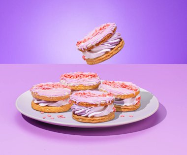 Değişik canlı hamur işleri ve pastalar, kruvasanlar, ekekler, kekler, mor arkaplan üzerinde yaratıcı bir şekilde havalanan çay saatinde dinamik çay serpintileri ve neşe katan elementler.