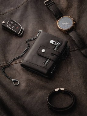 Zincirli lüks siyah cüzdan, zarif kol saati, şık bilezik ve zengin koyu dokulu deri yüzeye yerleştirilmiş araba anahtarı. Erkeklerin temel kavramı