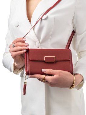 Koyu kırmızı deri çanta, altın aksanlı ve püsküllü beyaz elbiseli genç bayanın şık görünüşü. Lüks aksesuarlar ve kişisel zarafet kavramı