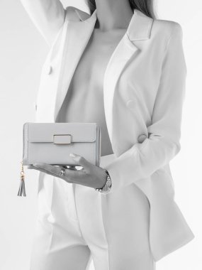 Tek renkli beyaz takım elbiseli, düğmesiz ceketli, vücudu teşhir eden altın sarısı ve püsküllü beyaz deri debriyaj tutan bir kadın resmi. Kısmi doygunluk etkisi olan biçimlendirilmiş fotoğraf