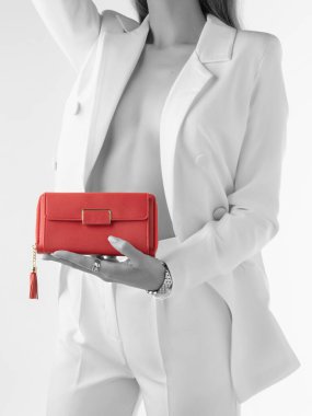 Tek renkli beyaz takım elbiseli, düğmesiz ceketli, vücudu teşhir eden altın rengi detaylar ve püsküllü kırmızı deri debriyaj tutan bir kadın resmi. Kısmi doygunluk etkisi olan biçimlendirilmiş fotoğraf