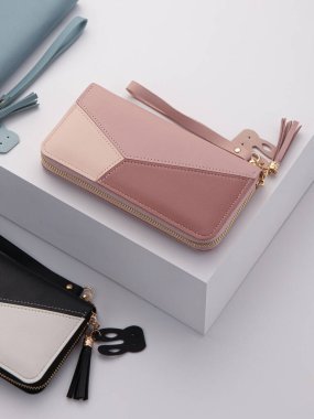 Pastel pembe ve çıplak renkte zarif kadın debriyajı geometrik desenli, altın fermuar, güvenli bileklik kayışı ve beyaz ayakta sunulan dekoratif püsküller.