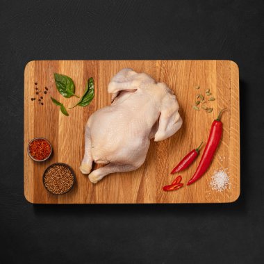 İştah açıcı, pişmeye hazır çiğ tavuk leşi, baharatlar ve sulamalarla kg grafit arka planda bir tahta üzerinde duruyor. 