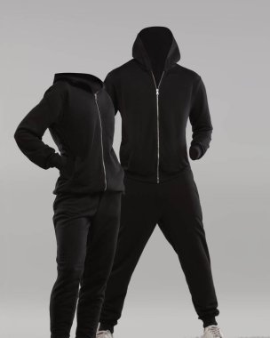 Basit bir arka planda siyah kapüşonlu ve eşofmanlı iki kafasız manken sergileniyor. Dikkatimizi kıyafet tasarımına ve dikkat dağıtmadan uyum sağlamaya vermeliyiz..