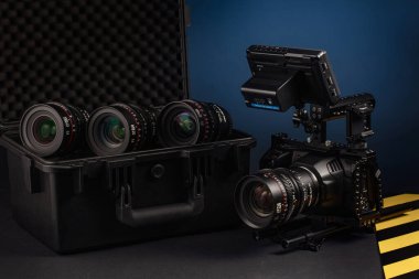 Profesyonel bir kamera teçhizatı karanlık bir masada hazır bekliyor. Yanında, bir stüdyoda çekim hazırlığını gösteren birkaç kamera lensi bulunan bir çanta var..