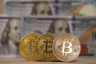 Almaty, Kazakistan - 04.04.2023: Bitcoin paraları arka planda 100 dolarlık banknotlara karşı durmaktadır.