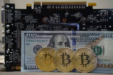 Almaty, Kazakistan - 04.04.2023: Dolar zemininde Bitcoin paralar ve bir video kartı.