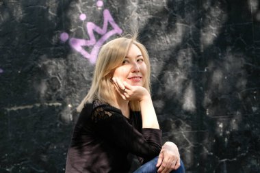 Genç bir kadın bir duvarın arkasında oturuyor. Üzerinde bir taç resmi var.