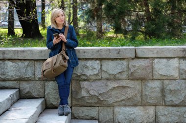 Seyahat çantası ve akıllı telefonu olan genç bir kadın merdivenlerde dikiliyor..