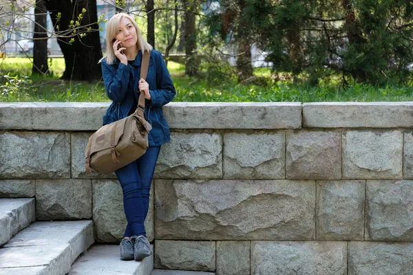 stock image A young woman with a travel bag and a smartphone is standing on the stairs.