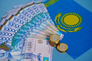 Masanın üzerine, Kazakistan bayrağının arka planına karşı onluk banknotlar ve sikkeler serilmiştir..