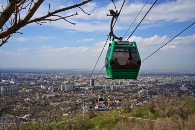 Almaty, Kazakistan - 04.07.2025: Turistlerle dolu bir kulübe şehrin üzerinde teleferiğe biniyor.