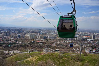 Almaty, Kazakistan - 04.07.2025: Turistlerle dolu bir kulübe şehrin üzerinde teleferiğe biniyor.