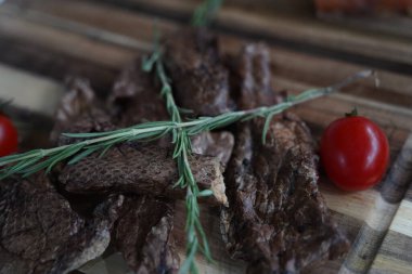 Pieces of dried smoked fish with rosemary and cherry tomatoes on a wooden board.