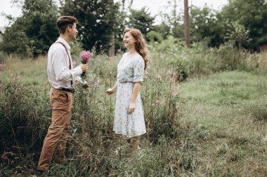 Tarz sahibi genç bir çift, kızın elini tutan, gülümseyen ve birbirine bakan bir erkek.