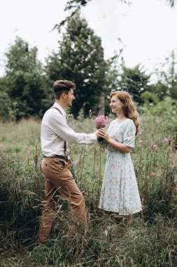 Tarz sahibi genç bir çift, kızın elini tutan, gülümseyen ve birbirine bakan bir erkek.