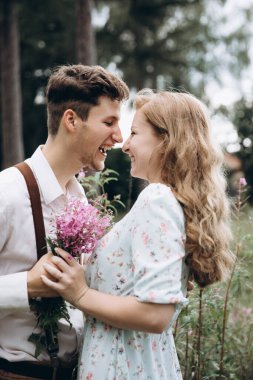 Tarz sahibi genç bir çift, kızın elini tutan, gülümseyen ve birbirine bakan bir erkek.